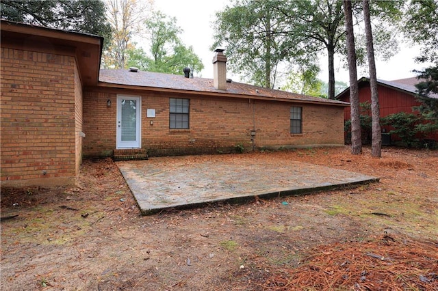 rear view of house featuring a chimney, a patio, and brick siding