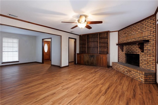 unfurnished living room featuring ceiling fan, hardwood / wood-style floors, ornamental molding, and a fireplace