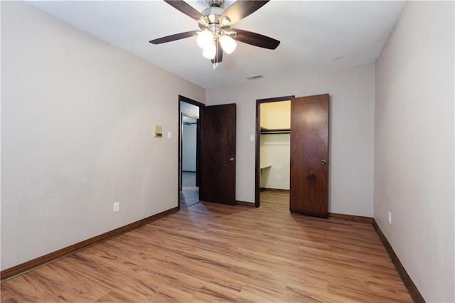 unfurnished bedroom with a closet, a walk in closet, ceiling fan, and light hardwood / wood-style flooring