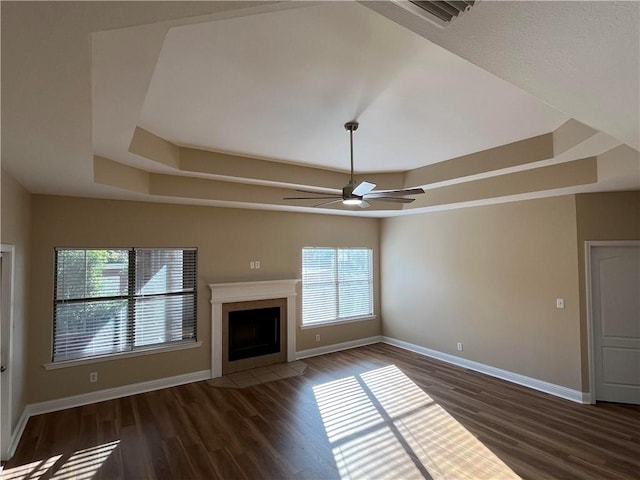 unfurnished living room featuring ceiling fan, a tray ceiling, and dark hardwood / wood-style floors