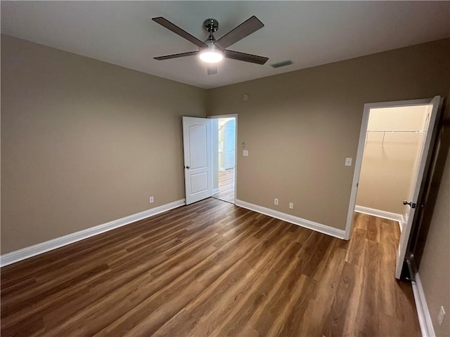 unfurnished bedroom with ceiling fan, a closet, dark wood-type flooring, and a walk in closet