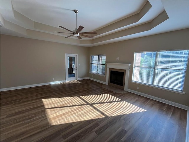 unfurnished living room with ceiling fan, dark hardwood / wood-style floors, and a raised ceiling