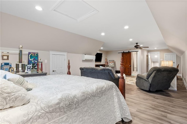 bedroom with vaulted ceiling, light hardwood / wood-style flooring, a barn door, and an AC wall unit