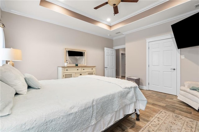 bedroom with light hardwood / wood-style flooring, a tray ceiling, ceiling fan, and ornamental molding