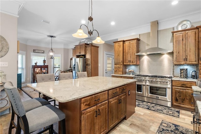 kitchen featuring pendant lighting, a kitchen island, wall chimney exhaust hood, appliances with stainless steel finishes, and decorative backsplash