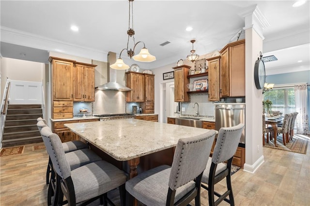 kitchen with sink, decorative light fixtures, light hardwood / wood-style flooring, backsplash, and wall chimney range hood