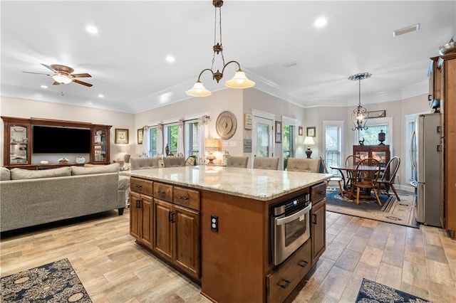 kitchen featuring pendant lighting, light hardwood / wood-style floors, ceiling fan with notable chandelier, a kitchen island, and appliances with stainless steel finishes