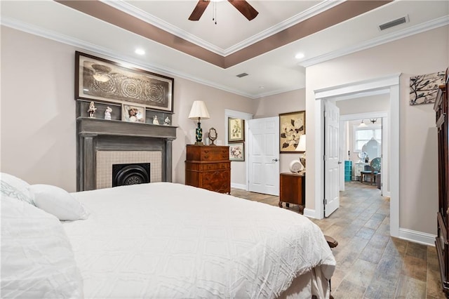 bedroom featuring wood-type flooring, a fireplace, ornamental molding, and ceiling fan