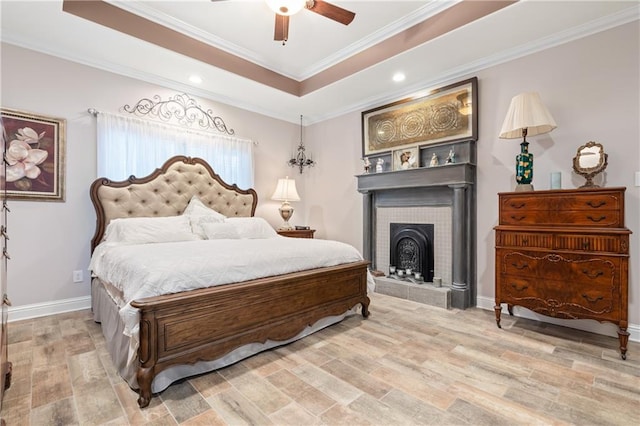 bedroom featuring ceiling fan, ornamental molding, a tray ceiling, a tile fireplace, and hardwood / wood-style floors