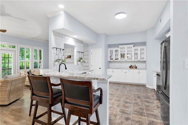 kitchen with white cabinetry, light stone counters, kitchen peninsula, a kitchen bar, and decorative backsplash