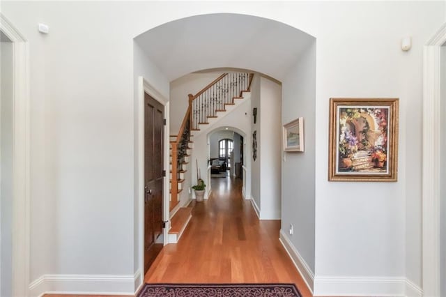 hall with stairway, baseboards, arched walkways, and wood finished floors