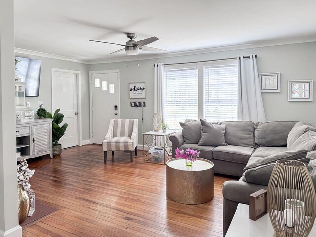 living room featuring a ceiling fan, crown molding, baseboards, and wood finished floors