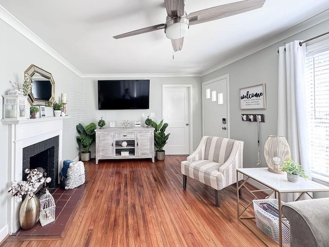 living room featuring a fireplace with flush hearth, crown molding, wood finished floors, and a ceiling fan