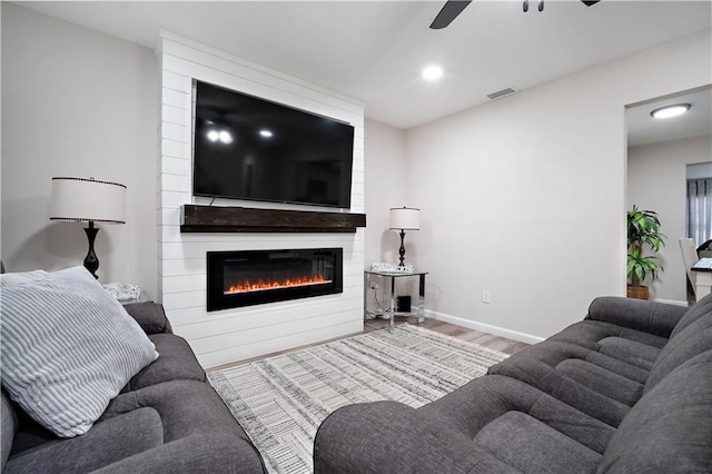living area featuring wood finished floors, baseboards, visible vents, a fireplace, and ceiling fan