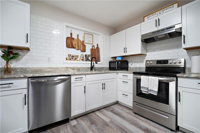 kitchen featuring decorative backsplash, under cabinet range hood, light wood-type flooring, and appliances with stainless steel finishes