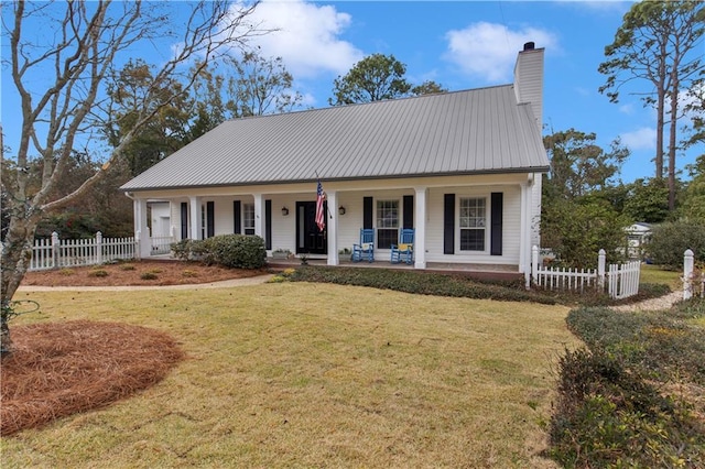 view of front of home featuring a chimney, covered porch, fence, metal roof, and a front lawn