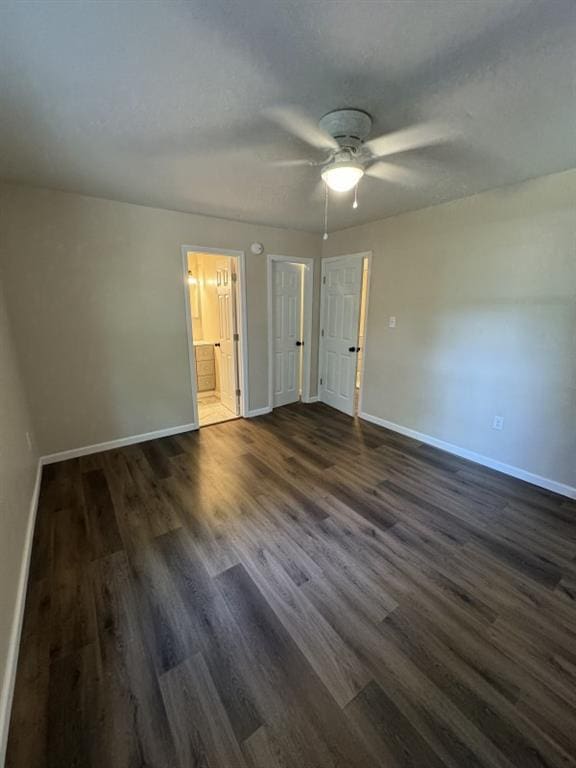 unfurnished bedroom with ensuite bathroom, ceiling fan, and dark wood-type flooring