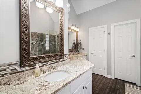 bathroom with vanity, decorative backsplash, hardwood / wood-style floors, and vaulted ceiling