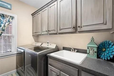 clothes washing area with plenty of natural light, cabinets, washing machine and clothes dryer, and sink