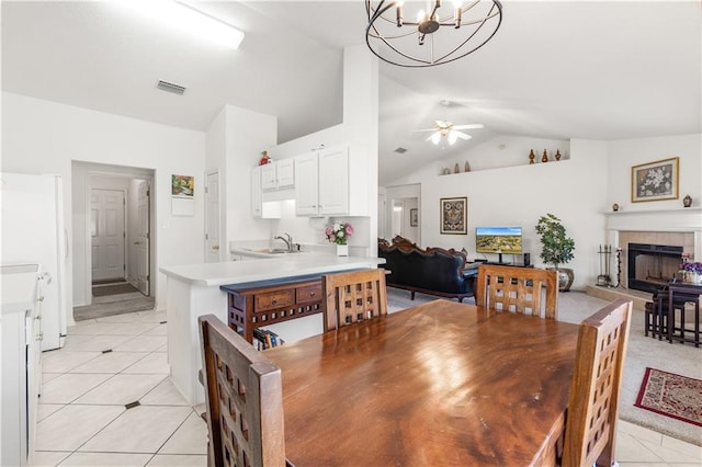 tiled dining space featuring lofted ceiling, ceiling fan with notable chandelier, a tiled fireplace, and sink