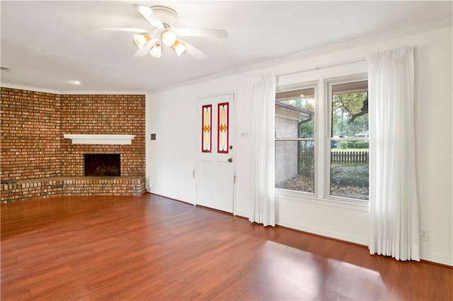 unfurnished living room featuring brick wall, ceiling fan, a fireplace, crown molding, and dark hardwood / wood-style flooring