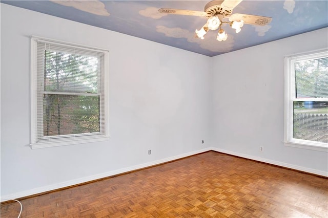 empty room with a wealth of natural light, parquet floors, and ceiling fan