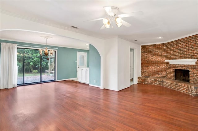 unfurnished living room with ceiling fan with notable chandelier, dark wood-type flooring, crown molding, a fireplace, and brick wall