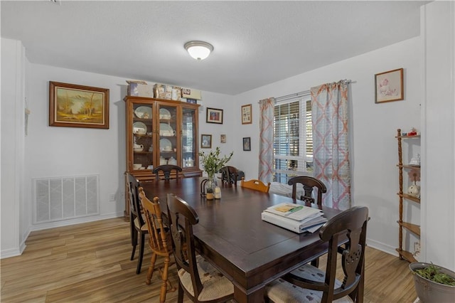 dining room with baseboards, a textured ceiling, visible vents, and light wood-style floors