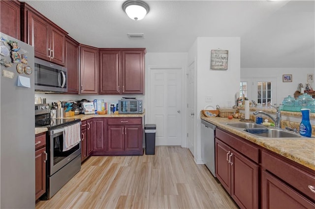 kitchen with reddish brown cabinets, visible vents, appliances with stainless steel finishes, and a sink