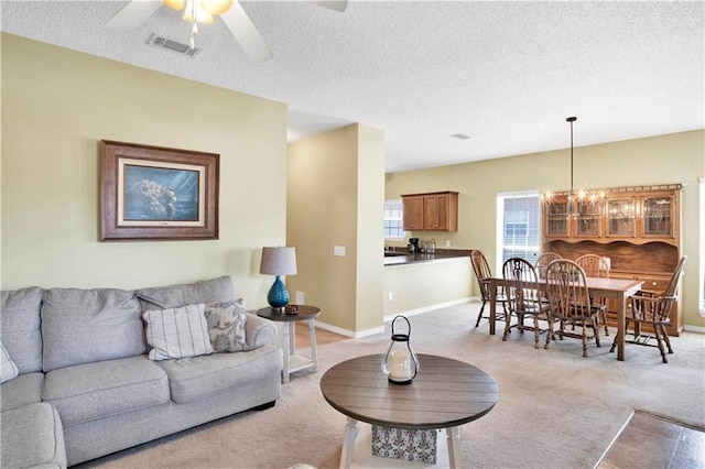 living room with light carpet, ceiling fan with notable chandelier, and a textured ceiling