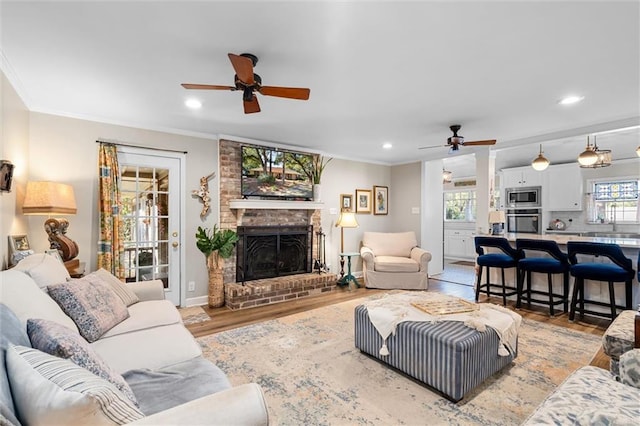 living room with a brick fireplace, light hardwood / wood-style flooring, ceiling fan, and crown molding