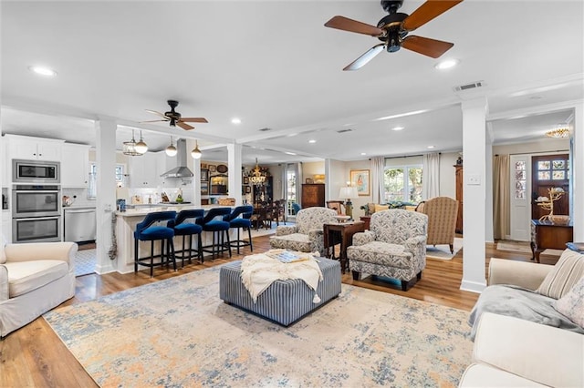 living room with ornate columns, light hardwood / wood-style flooring, ceiling fan with notable chandelier, and ornamental molding