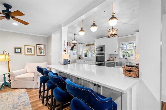 kitchen featuring a breakfast bar, decorative light fixtures, stainless steel appliances, and white cabinetry