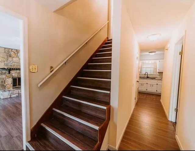 stairs featuring wood-type flooring, a stone fireplace, and sink