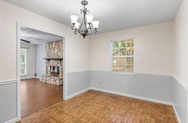 unfurnished room with a stone fireplace, a textured ceiling, a wealth of natural light, and a chandelier