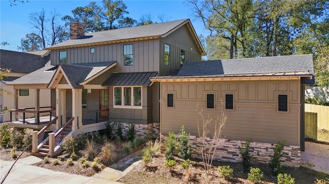 view of front of house featuring stone siding, a sunroom, a chimney, board and batten siding, and a shingled roof