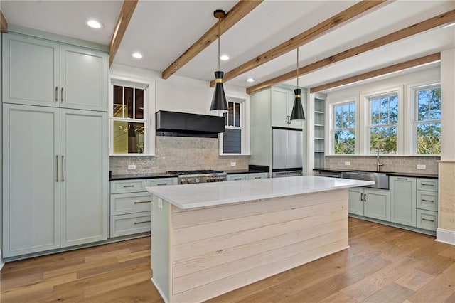 kitchen featuring dark stone counters, stainless steel appliances, beam ceiling, a sink, and exhaust hood