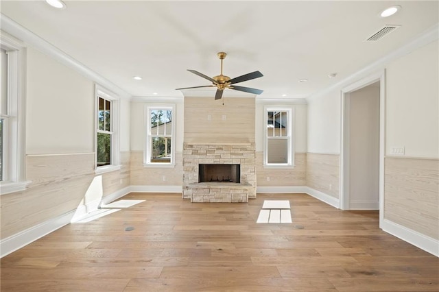 unfurnished living room with light wood-type flooring, ceiling fan, crown molding, and a stone fireplace