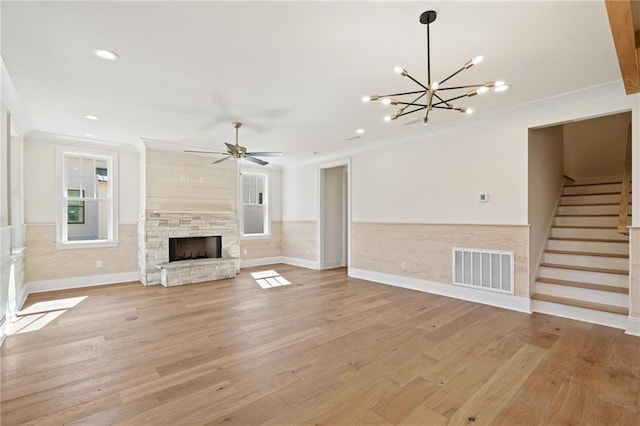 unfurnished living room with light wood-type flooring, crown molding, a fireplace, and ceiling fan with notable chandelier