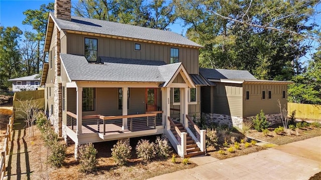 view of front of property featuring stone siding, board and batten siding, covered porch, a shingled roof, and a chimney