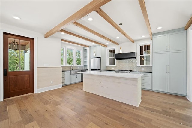 kitchen featuring ventilation hood, beam ceiling, hanging light fixtures, white fridge, and light hardwood / wood-style flooring