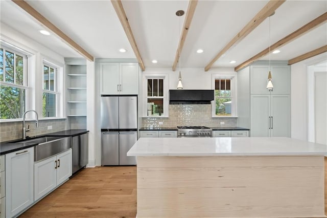 kitchen with dark stone counters, light wood-type flooring, beam ceiling, stainless steel appliances, and decorative light fixtures