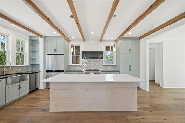 kitchen featuring stainless steel appliances, a kitchen island, a sink, beamed ceiling, and light wood finished floors