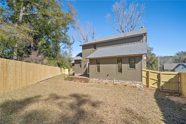 back of property with a shingled roof, a fenced backyard, board and batten siding, and a gate