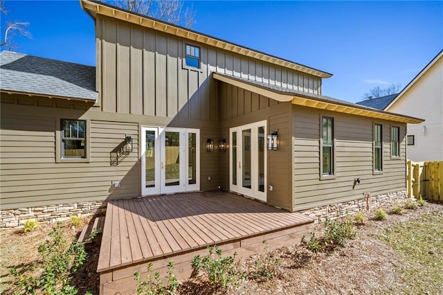 back of property with french doors, roof with shingles, a wooden deck, fence, and board and batten siding
