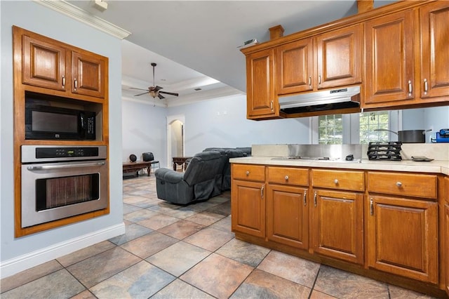 kitchen with ceiling fan, oven, light tile patterned flooring, a tray ceiling, and ornamental molding