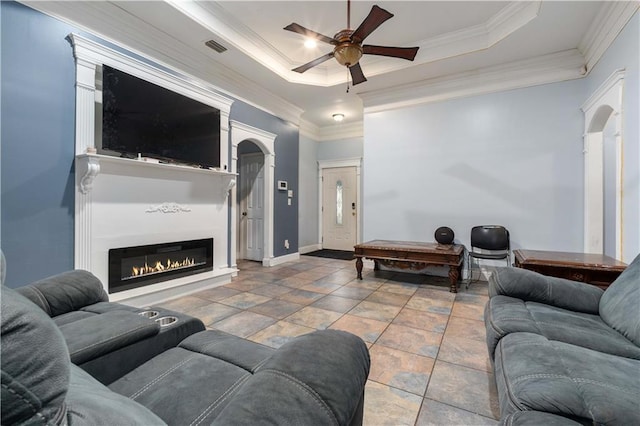 tiled living room with a raised ceiling, crown molding, and ceiling fan