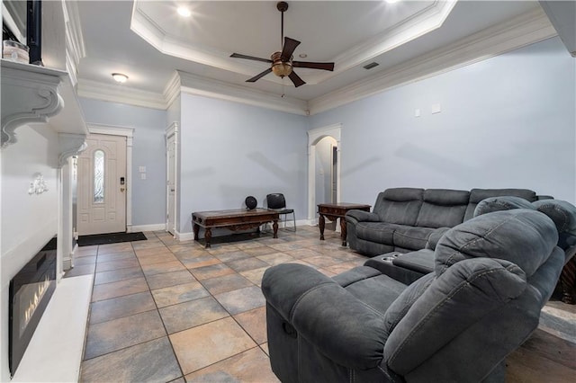 living room with ceiling fan, tile patterned flooring, a tray ceiling, and ornamental molding