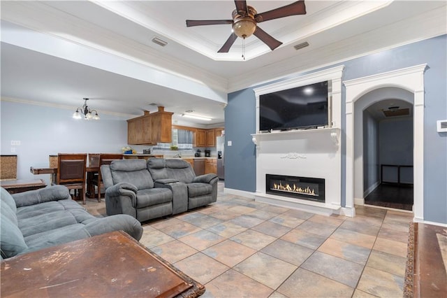 tiled living room with ceiling fan with notable chandelier, crown molding, and a tray ceiling