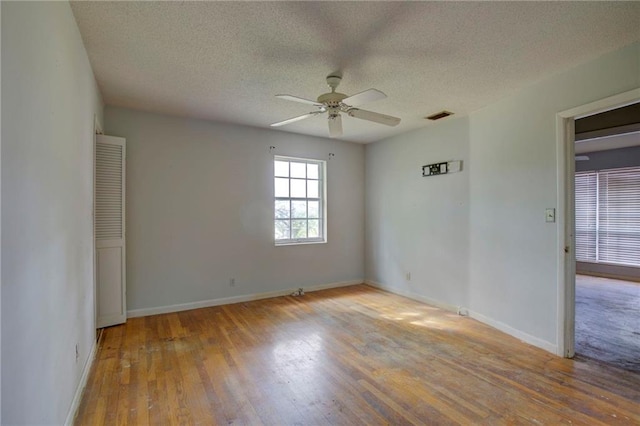 empty room with ceiling fan, light wood-type flooring, and a textured ceiling